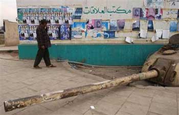 An Iraqi man walks past the remains of an old tank and a wall covered with elections posters, in Baghdad, Monday, Jan. 17, 2005. The election planned for Jan. 30 is the first democratic vote in Iraq since the country was formed in 1932. Iraqi officials announced Tuesday that they will close the nation's borders, extend nighttime curfews and restrict internal movement to protect voters during the Jan. 30 elections. [AP] 