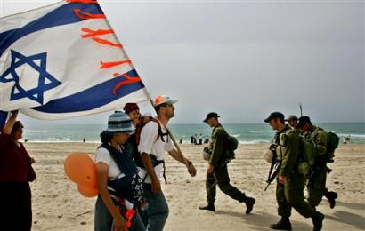 Israeli soldiers on patrol walk past Israelis as Jewish settlers and opponents of Israel's planned withdrawal from the Gaza Strip march along the beach near the settlement of Nve Dekalim in the Gush Katif bloc of settlements, southern Gaza Strip Wednesday April 27, 2005. Thousands of Jewish settlers and their supporters poured into the area Wednesday to join a protest against Israeli Prime Minister Ariel Sharon's plan to withdraw from the Gaza Strip and four West Bank settlements this summer. The orange color has been adopted by the opposers to Prime Minister Ariel Sharon's plan to pull out of the Gaza Strip. (AP