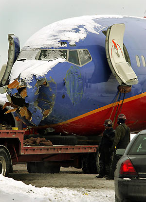 jWorkers survey the Southwest Airlines plane as it sits on a truck after being removed from a busy street bordering Chicago's Midway Airport December 10, 2005. The plane skidded off a snowy runway and onto adjacent streets during a snowstorm on Thursday evening, killing a child riding in a car and came to rest atop two vehicles in the road. 