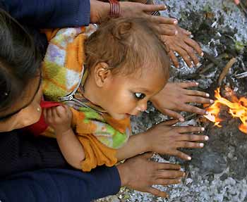 A homeless Indian migrant worker sits with her child beside a bonfire by a road in the northern Indian city of Chandigarh January 9, 2006.