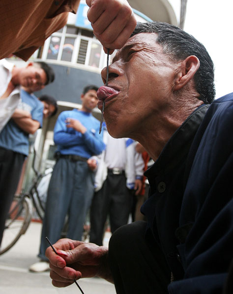 A stuntman allows a man to pull iron wire through his tongue in Foshan, South China's Guangdong Province April 6 2006. The stuntman was performing for donations for his daughter's college tuition. He said farming alone couldn't provide enough for the education costs. 